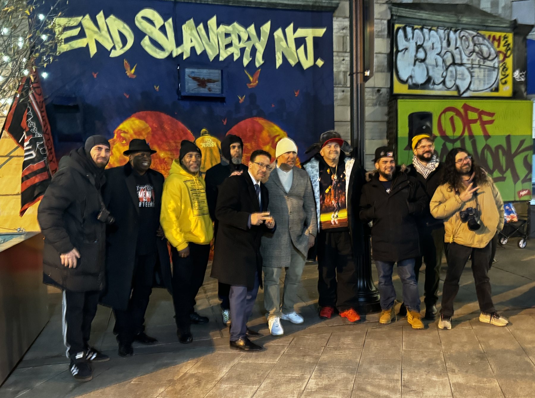 Organizers, the artist, and supporters standing in front of the End Slavery NJ mural at night